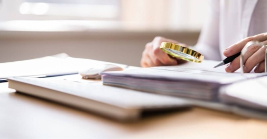 LOOKING AT PAPERWORK WITH MAGNIFYING GLASS